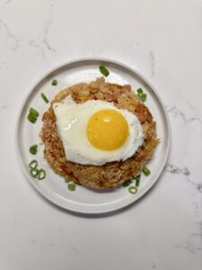 Kimchi fried rice with Spam topped with fried egg and scallions in a white bowl