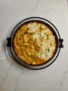 Close-up of rose tteokbokki in a skillet topped with melted mozzarella and chopped green onions.