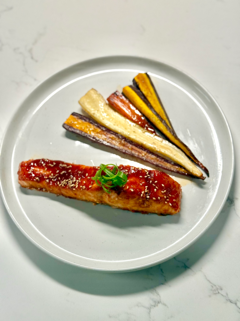 Oven-baked gochujang salmon fillet topped with sesame glaze and paired with rainbow carrots on a plate