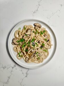 A bowl of creamy mushroom udon topped with sliced green onions and sesame seeds on a white countertop.