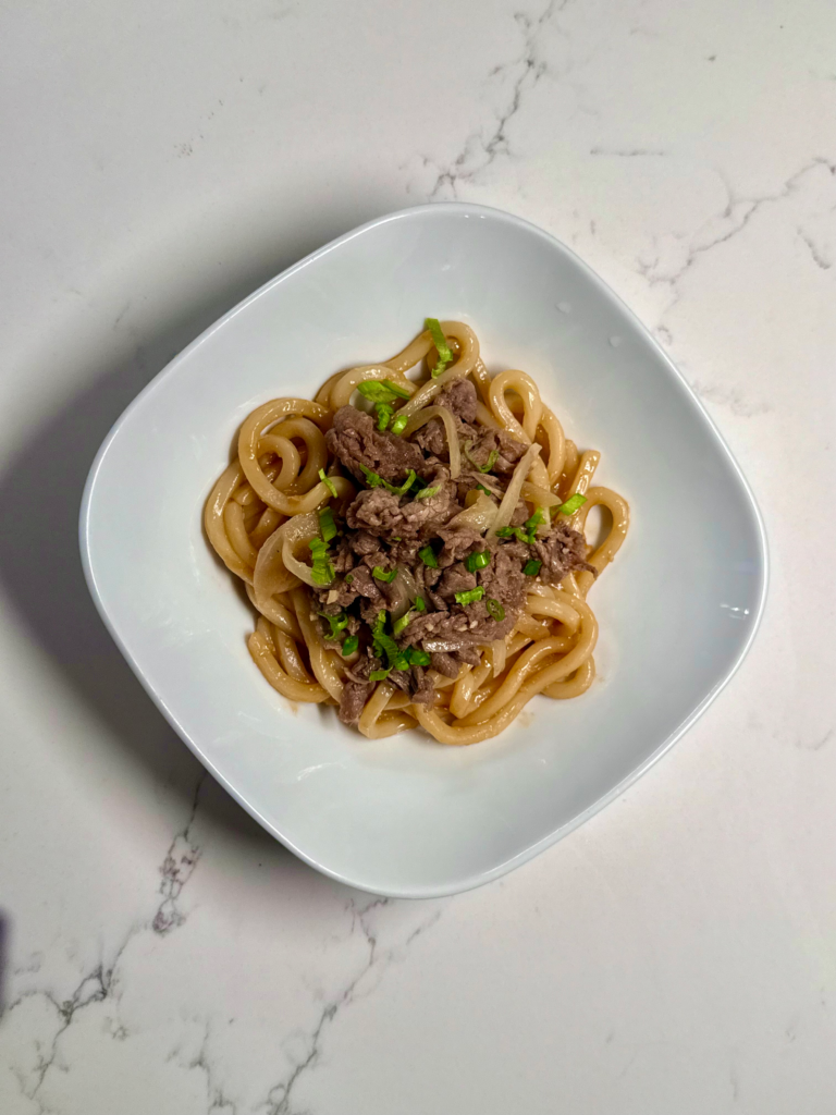 Overhead shot of a bowl of beef sukiyaki udon with caramelized beef and green onions on top.