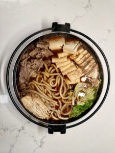 Overhead view of finished sukiyaki hotpot in a black bowl, filled with beef, tofu, noodles, and vegetables for an authentic Japanese beef hotpot recipe.
