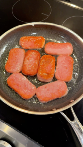 Pan-searing Spam slices in a skillet until golden and crispy on both sides for the musubi