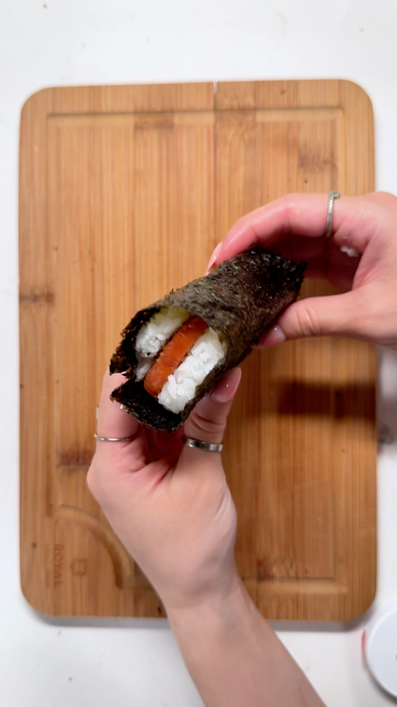 Wrapping a strip of nori seaweed around the musubi to hold its shape and add flavor