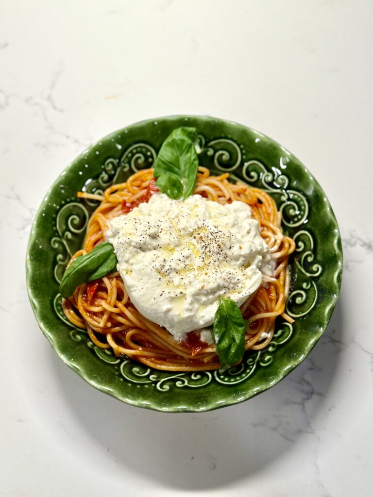 Plated spaghetti with burrata on top, garnished with basil and crispy pancetta.