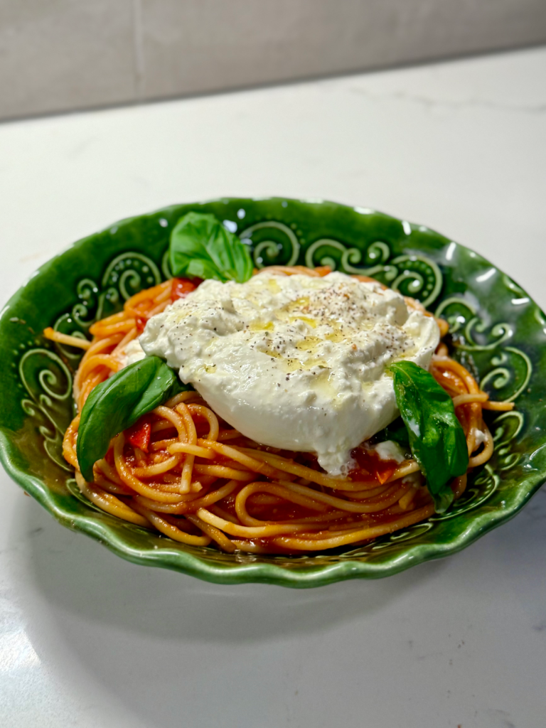 Close-up of burrata melting into warm spaghetti with tomato sauce and pancetta.