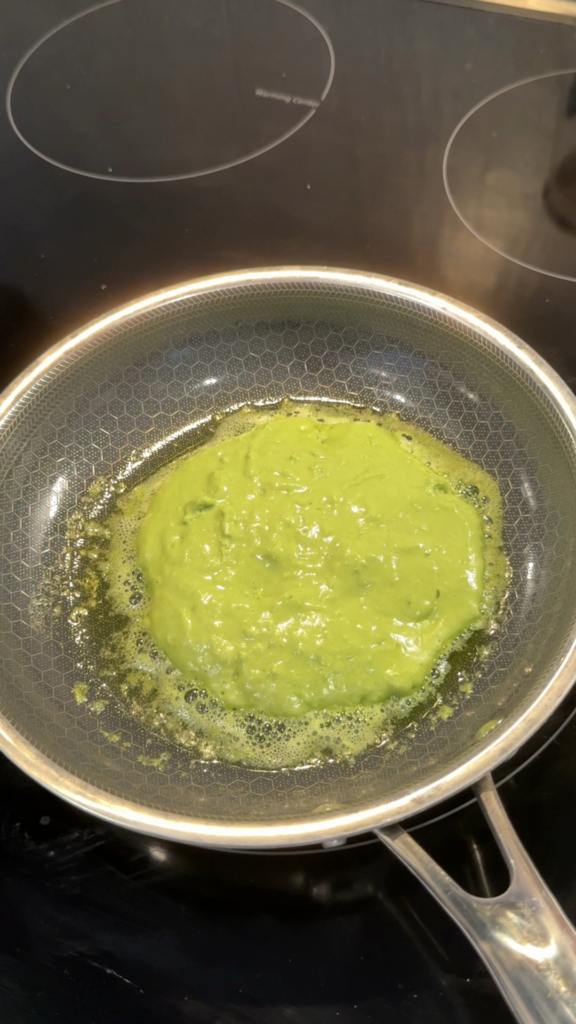 Matcha pancake batter cooking on a nonstick pan with small bubbles forming on the surface.