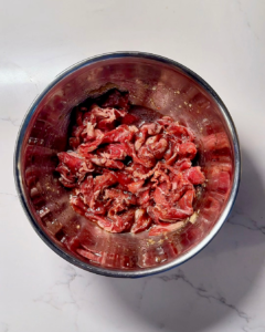 Thinly sliced sukiyaki beef marinating in a bowl with onions and sauce.