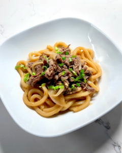 Plated beef sukiyaki udon topped with green onions and sesame seeds.