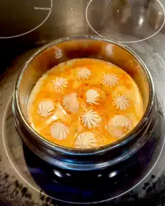 Soup dumplings simmering in spicy tom yum broth in a hot stone pot, photographed mid-cook with gentle bubbling around the edges.