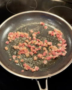 Pancetta sizzling and turning golden in a pan to prepare spaghetti with burrata.