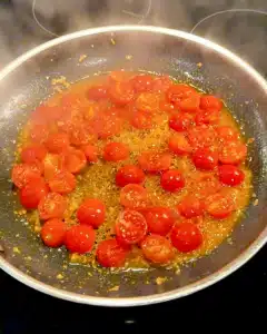 Cherry tomatoes cooking in olive oil, starting to blister for burrata spaghetti sauce.