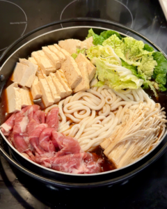 Uncooked sukiyaki ingredients arranged beautifully in a shallow hotpot pan, including thinly sliced beef, tofu, mushrooms, and cabbage before simmering.