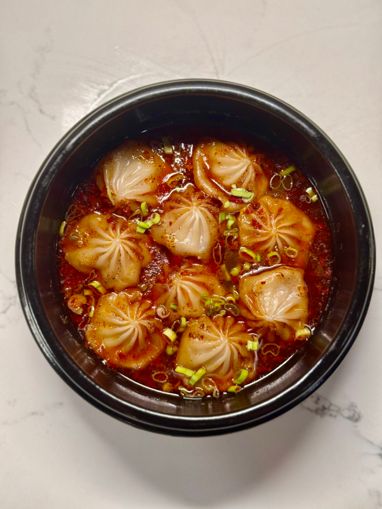 Hot mala soup dumplings served in dolsot with chili crisp, green onion, and sesame seeds