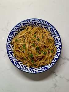 Bowl of glossy Shanghai-style scallion oil noodles tossed in soy sauce and sesame seeds, topped with green onions and served on a marble surface.