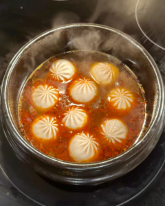 Frozen xiao long bao simmering in spicy mala soup broth inside a stone pot