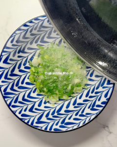 Hot oil being poured from a pan over fresh chopped scallions in a bowl, creating a sizzling aroma — key step in making authentic scallion oil noodles.