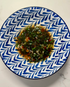 Overhead view of finely chopped scallions mixed with soy sauce, sugar, and oil in a blue patterned bowl — the aromatic base for Shanghai-style scallion oil noodles.